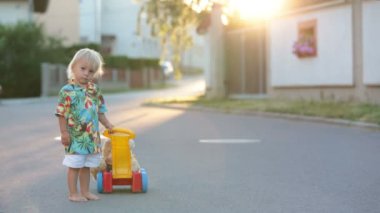 Güzel çocuk, plastik oyuncaklarla, bloklarla, küçük bir köyde gün batımında arabalarla oynuyor.