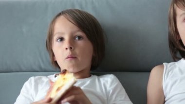 Tatlı çocuklar, kanepede oturuyor, pizza yiyor ve televizyon seyrediyorlar. Evde pizza günü pizza yiyen aç bir çocuk.