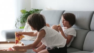Tatlı çocuklar, kanepede oturuyor, pizza yiyor ve televizyon seyrediyorlar. Evde pizza günü pizza yiyen aç bir çocuk.