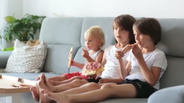 Tatlı çocuklar, kanepede oturuyor, pizza yiyor ve televizyon seyrediyorlar. Evde pizza günü pizza yiyen aç bir çocuk.