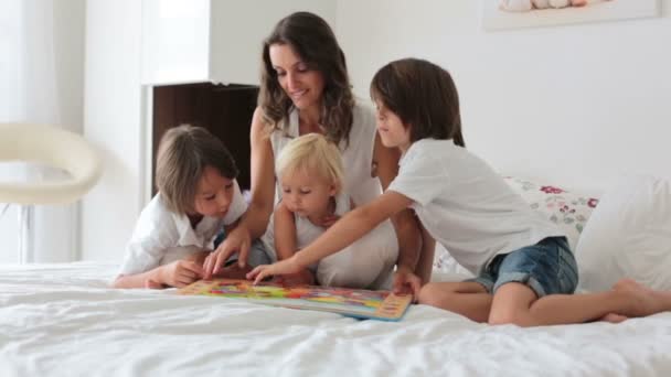 年轻的母亲 读一本书给她的三个孩子 男孩在阳光明媚的卧室在家里 — 图库视频影像