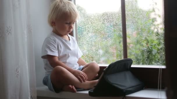 Adorable Niño Sentado Escudo Ventana Jugando Tableta Día Lluvioso Verano — Vídeo de stock