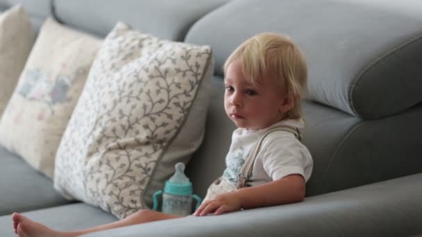 可爱的男婴在一个阳光灿烂的白色客厅里喝着一瓶牛奶 婴儿配方饮料 — 图库视频影像