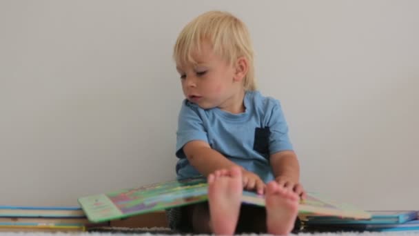 甘い幼児の少年 自宅で本を読んで 地面に座って 彼の周りの本の多く — ストック動画