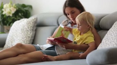 Sevimli anne, evde vişne yiyen küçük bebeğine bir kitapta resimler gösteriyor.