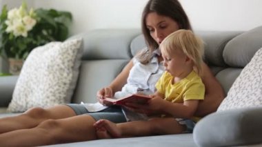 Sevimli anne, evde vişne yiyen küçük bebeğine bir kitapta resimler gösteriyor.