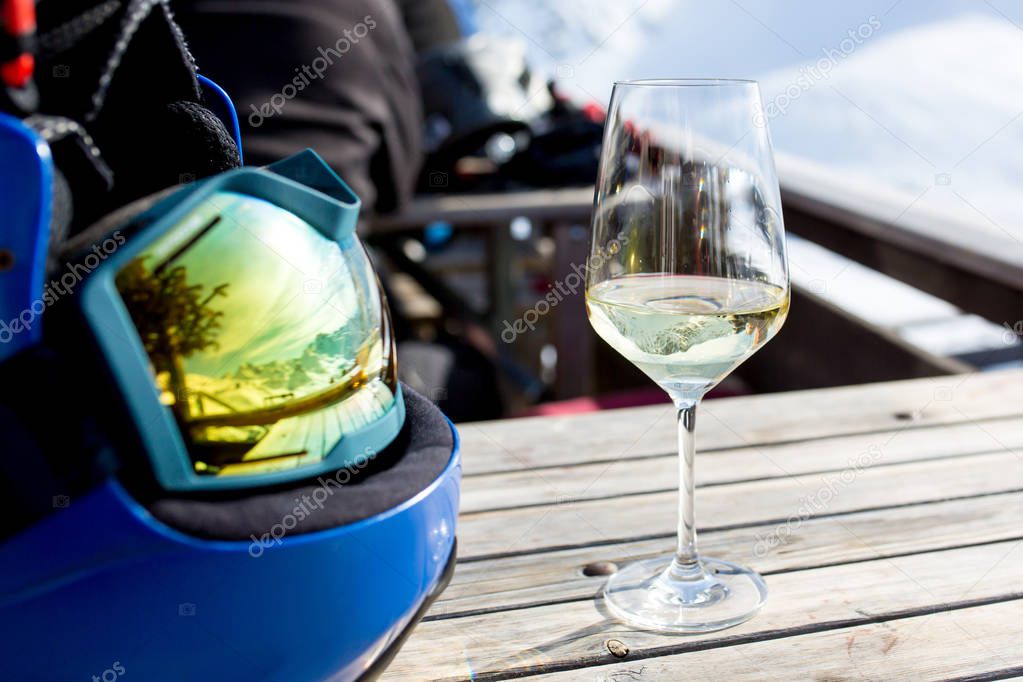 Reflections of snowy mountain in helmet and a glass of wine on t