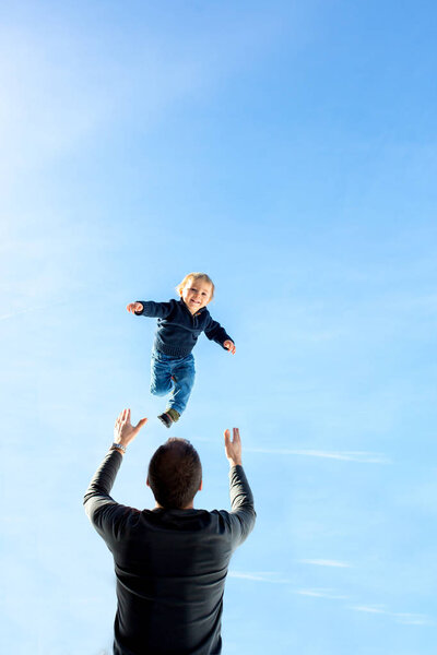 Little toddler boy, flying in the sky, dad throwing him high in 