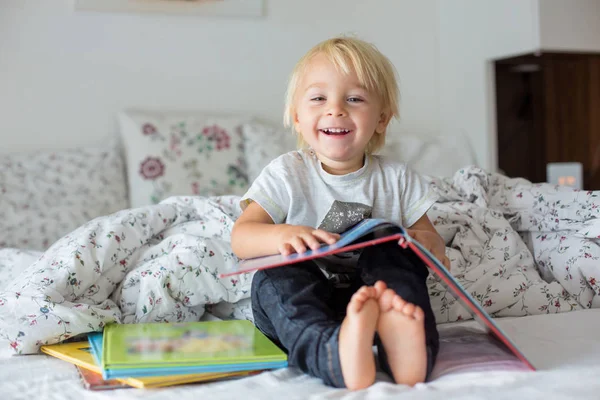 Sweet toddler boy, reading book at home, sitting in bed, lots of — Stock Photo, Image