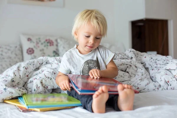 Sweet toddler boy, reading book at home, sitting in bed, lots of — Stock Photo, Image