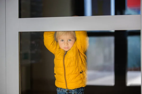 Blond malé batole dítě ve žluté bundě, hraje si za — Stock fotografie