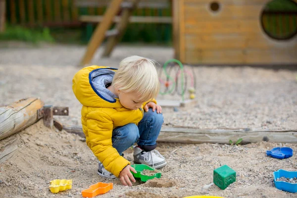 Blond liten barn i gul jacka, leker på pla — Stockfoto