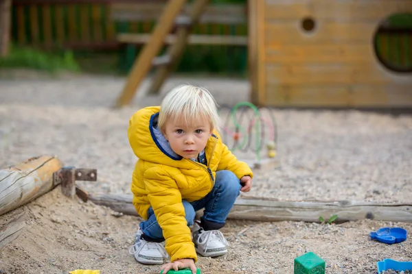 Blond peuterkindje in geel jasje, spelend op de pla — Stockfoto