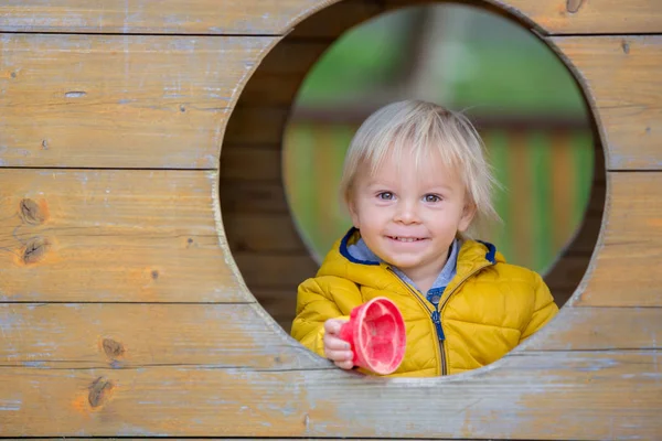 Blond peuterkindje in geel jasje, spelend op de pla — Stockfoto