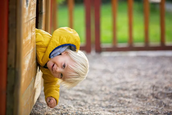 Blonde little toddler child in yellow jacket, playing on the pla — Stock Photo, Image