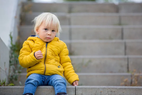 Blond małe dziecko w żółtej kurtce, bawiące się na pla — Zdjęcie stockowe