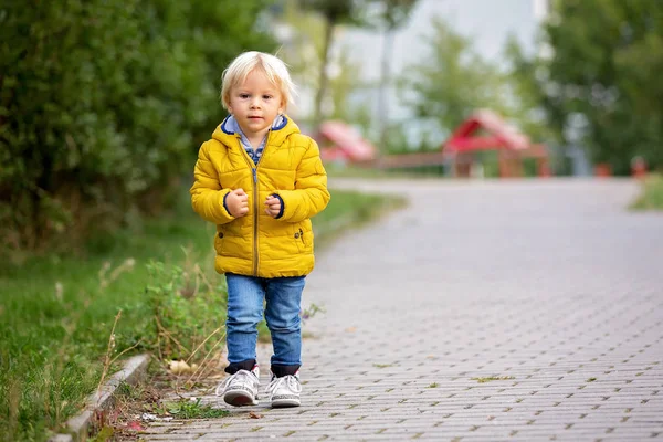 Blond liten barn i gul jacka, leker på pla — Stockfoto