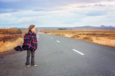Güzel çocuk, çok rüzgarlı bir günde yolda duruyor, sarılmış.