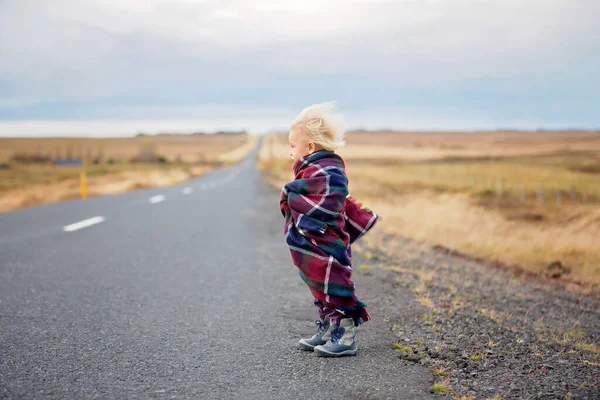 Hermoso niño, de pie en un camino en un día muy ventoso, envuelto —  Fotos de Stock