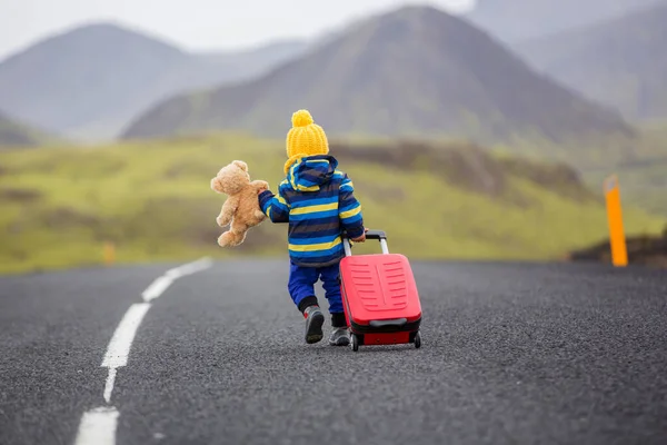 Söt liten pojke med nalle och resväska i handen, kör o — Stockfoto