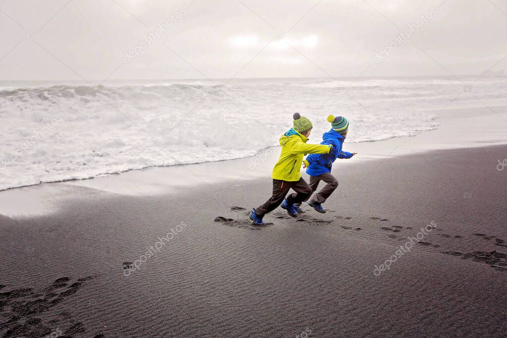 Children running from and to the ocean in black sand beach of Re
