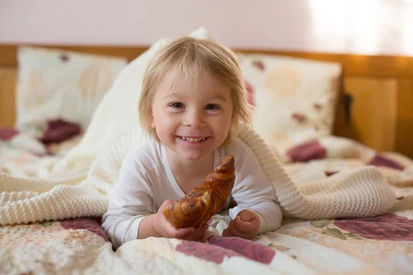 Criança Loira Bonito Ler Livro Comer Croissant Cama Rindo Alegremente — Fotografia de Stock