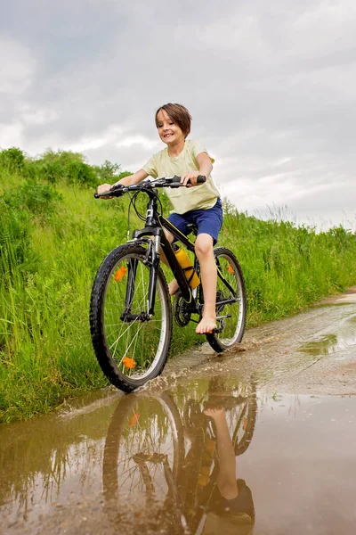 男の子 泥だらけの水たまりの中で自転車に乗る 雨の日の夏時間 — ストック写真