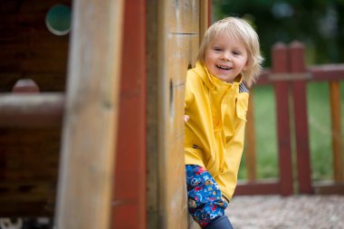 Tatlı çocuk, sarışın çocuk, baharda, bulutlu bir günde oyun parkında oynuyor.