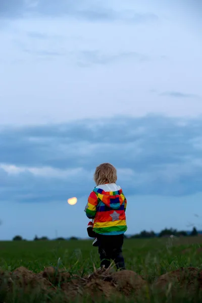 幸せな子供 手にスニーカーのペアを保持し 月明かりの下でフィールドを歩いて 満月が空に上昇 — ストック写真