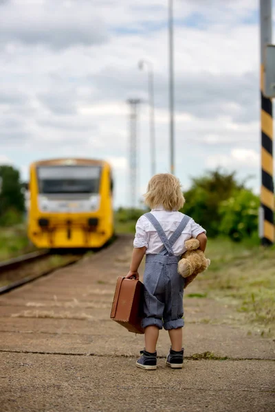 可爱的幼儿 带着玩具熊 书本和老式手提箱 在火车站等火车 准备放暑假 — 图库照片