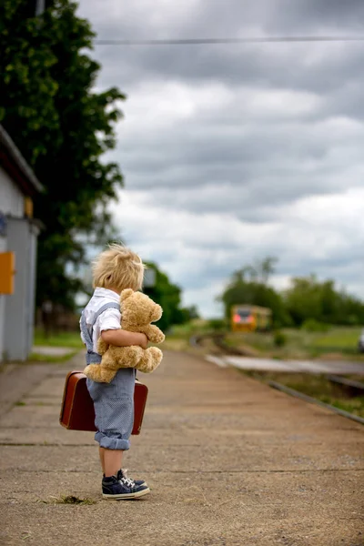 甘いです幼児子供とともにテディベア 電車の駅で電車を待っている本とヴィンテージスーツケース 夏休みに行く — ストック写真
