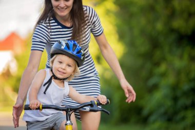 Genç anne, oğluna bisiklet sürmeyi öğretiyor, ona sarılıyor ve bisiklete binmeyi öğretiyor.