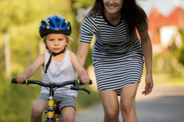 Genç anne, oğluna bisiklet sürmeyi öğretiyor, ona sarılıyor ve bisiklete binmeyi öğretiyor.