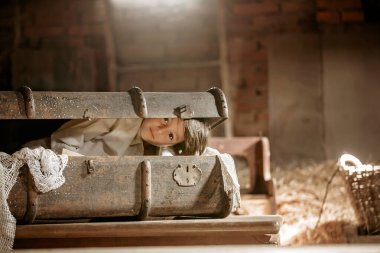 Küçük çocuk, çocuk, tavan arasında eski bir bavulda saklanıyor, bulunamamaktan korkuyor.