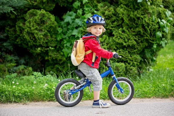 青いヘルメットとかわいい幼児の男の子 路上でバランス自転車に乗る 背景がぼやけて — ストック写真