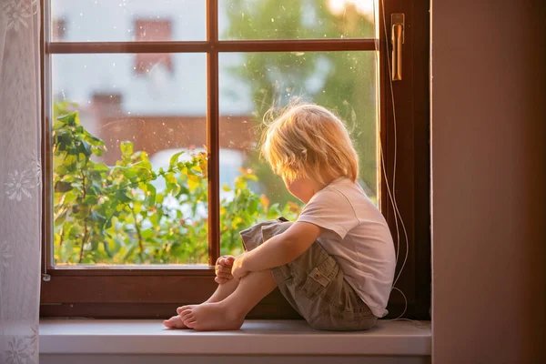 忘れられた小さな幼児の少年は 窓の盾の上に悲しい座って 日没を外を見る — ストック写真