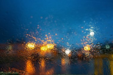 Geceleri arkasında ışıklar olan bir pencereye yağmur damlaları düşer.