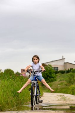 Çocuk, çocuk, çamurlu su birikintisinde bisiklete binmek, yağmurlu bir günde yaz zamanı