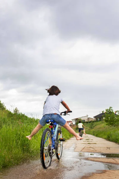 男の子 泥だらけの水たまりの中で自転車に乗る 雨の日の夏時間 — ストック写真