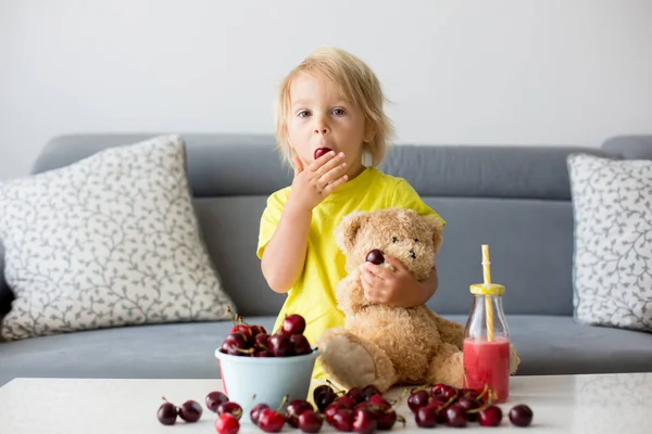 一个金发碧眼的孩子 可爱的男孩 在家里和泰迪熊一起吃樱桃 — 图库照片