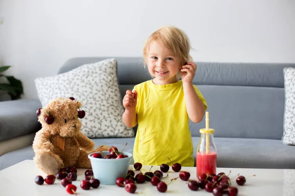 幼児ブロンド子供 かわいい男の子 食べるチェリーとともにテディベアとともに自宅 — ストック写真