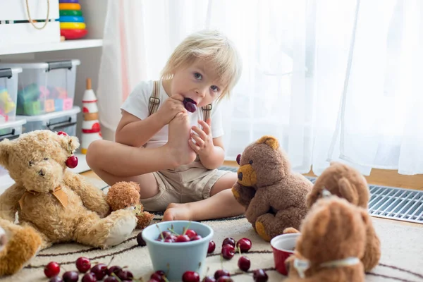 一个金发碧眼的孩子 可爱的男孩 在家里和泰迪熊一起吃樱桃 — 图库照片