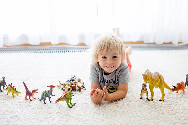 Blond toddler child, playing with dinosaurs at home, nice soft back light