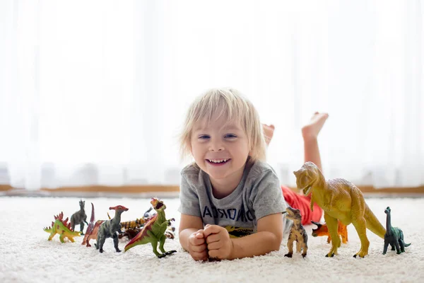 ブロンドの幼児の子供 自宅で恐竜と遊ぶ 素敵な柔らかいバックライト — ストック写真