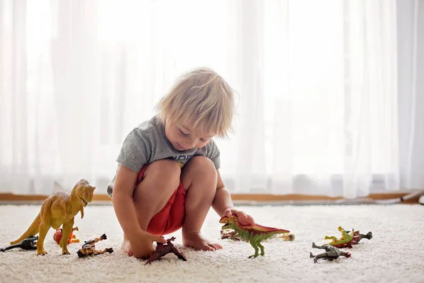ブロンドの幼児の子供 自宅で恐竜と遊ぶ 素敵な柔らかいバックライト — ストック写真