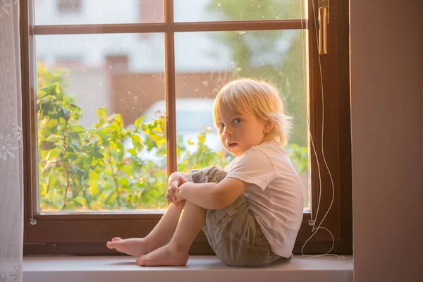 忘れられた小さな幼児の少年は 窓の盾の上に悲しい座って 日没を外を見る — ストック写真