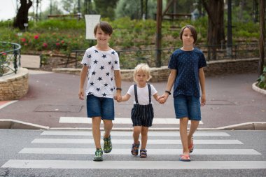 Children, boy brothers, siblings holding hands and crossing crosswalk on the street, summertime