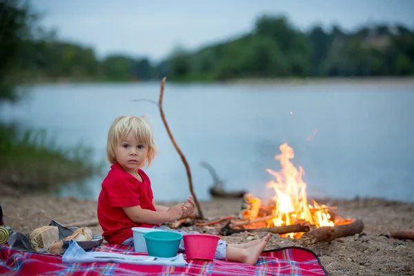 幼児男の子 子供がピクニックをしている彼の家族とキャンプファイヤー川の夏の近くの夜 — ストック写真