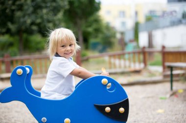 Parkta oynayan sevimli çocuk, mavi balığın salıncağında sallanıyor.