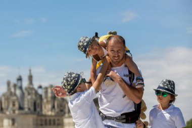 Baba, oğlunu boynuna takıyor, diğer iki oğluyla birlikte parkta yürüyor.